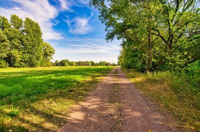 Empty road amidst field against sky