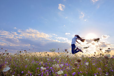 Side view full length of teenage girl jumping on flowering field