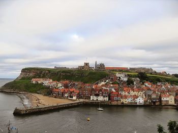 City at waterfront against cloudy sky