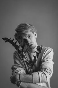 Portrait of young man holding plant against gray background