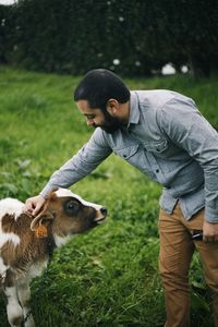 Side view of man stroking calf on field