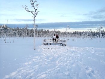 People sitting on bench against sky during winter