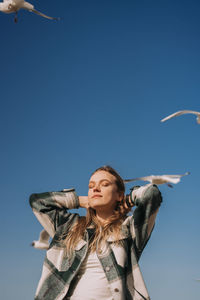 Low angle view of woman flying against clear blue sky