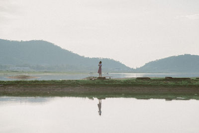 Full length of young woman standing by water against sky