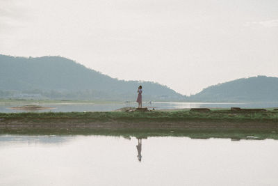 Woman standing by lake against sky