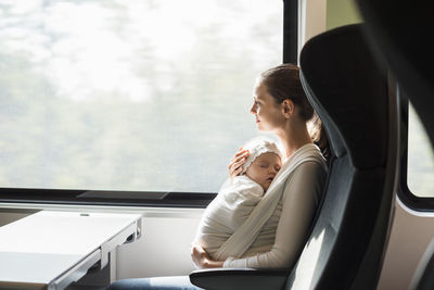 Mother with baby girl traveling by train looking out of window