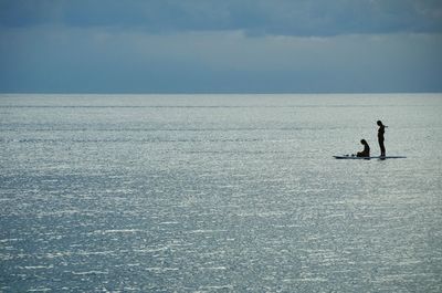 Women paddleboarding in sea against sky