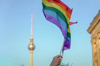 Low angle view of hand holding rainbow flag against sky