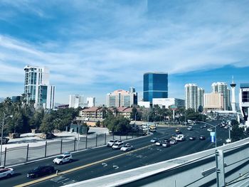 Vehicles on road by buildings against sky in city