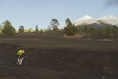 Female cyclist riding on dirt track with snowy mount teide in back