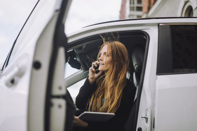 Businesswoman talking on smart phone while disembarking from car