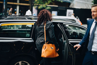 Businessman holding door while businesswoman entering taxi in city