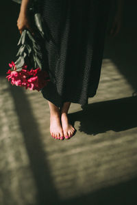 Low section of woman standing on lighted floor and holding bouquet of pink flowers