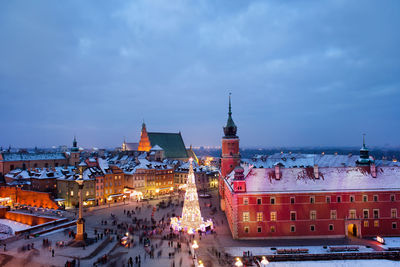 People by decorated illuminated christmas tree by church at town square against sky