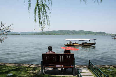 Rear view of people sitting on bench by lake