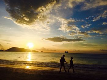 Silhouette people on beach against sky during sunset