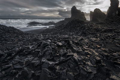 Rock formations by sea against cloudy sky