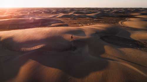 Aerial view of desert dunes with a man walking alone across a vast desert at sunset