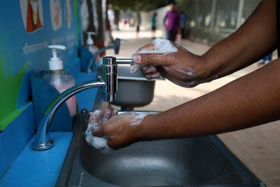 Close-up of hand holding faucet in water at home