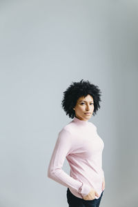 Portrait of confident businesswoman with hands in pockets standing against wall in office