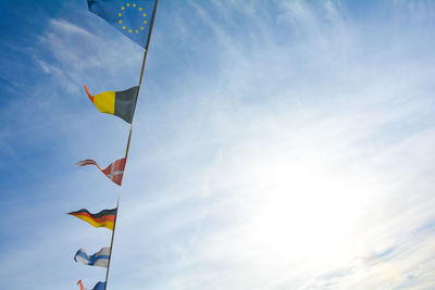 Flags from several different countries hang from a rope, against a lot of blue sky