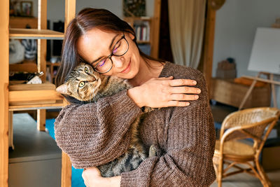 Middle-aged woman hugging cute tabby cat in indoor scene. human-animal relationships. funny home pet