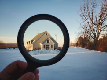 Close-up of hand holding magnifying glass against sky