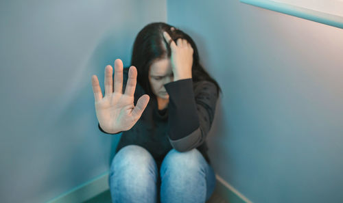 Depressed woman sitting by wall at home