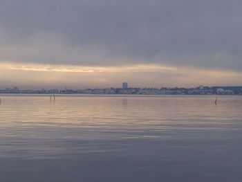 View of city at waterfront against cloudy sky