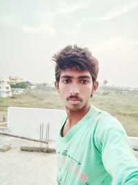 Portrait of young man standing on land against sky