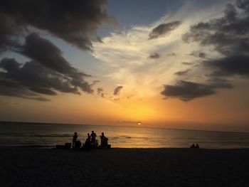 Silhouette people on beach against sky during sunset