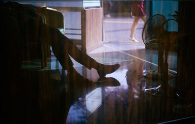 Low section of man sitting on chair seen through glass