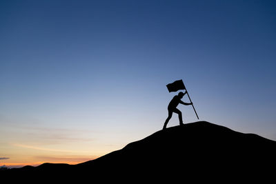 Silhouette man standing on mountain against clear sky during sunset