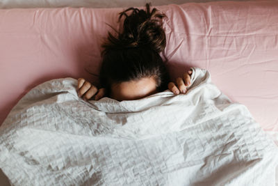 Woman covered in blanket lying on bed