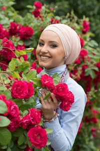 Portrait of smiling woman standing by red flowers growing on plant