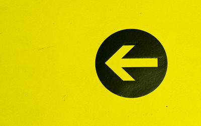 Close-up of arrow sign on yellow wall
