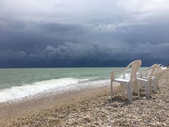 Empty chairs at beach against cloudy sky