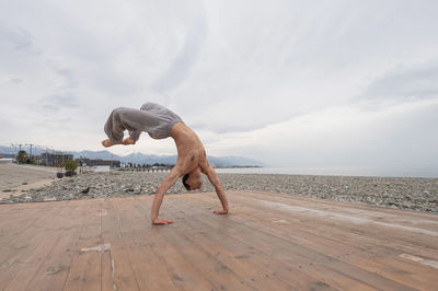 Full length of woman exercising at beach against sky