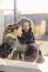 Happy female university students using digital tablet on subway station