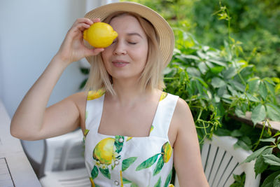 A girl in a straw hat sits on a terrace with green plants in summer