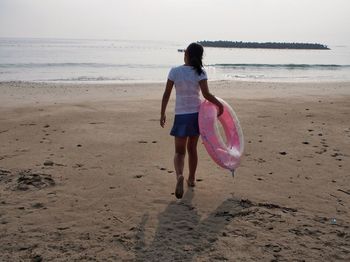 Rear view full length of girl walking with inflatable ring at beach