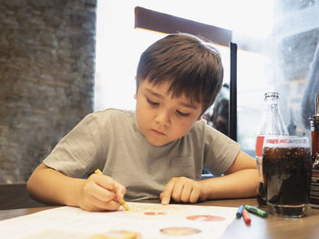 Cute boy painting while sitting on table