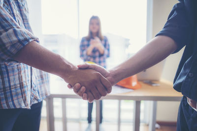 Midsection of men handshaking while standing indoors