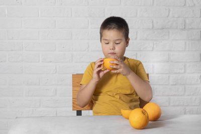 Portrait of young woman holding apple while standing against wall