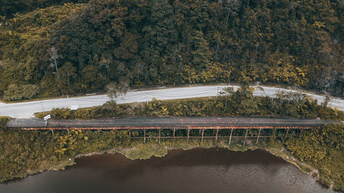Aerial view of the an old metal bridge crossing in between the road and the lake near the big forest