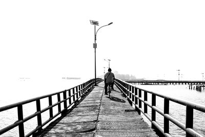 Man standing on railing by sea against clear sky
