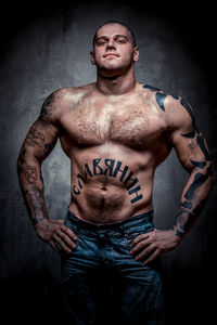 Portrait of shirtless muscular man with tattoos standing against gray background