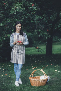 Full length portrait of smiling woman holding fresh apples at orchard