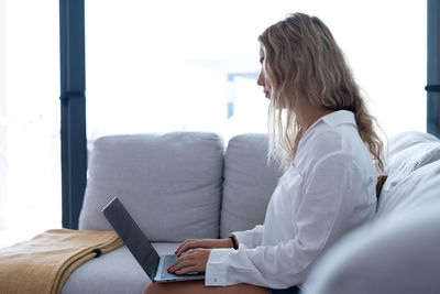 Side view of woman using mobile phone while sitting on bed at home