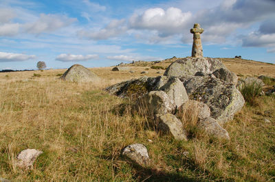 Panoramic view of rocks and cross on field against sky